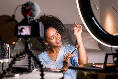 Young influencer vlogging about make-up product sitting at home