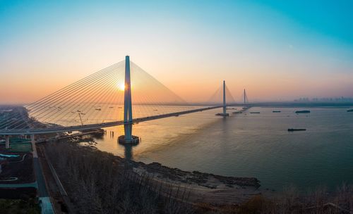 Suspension bridge over sea during sunset