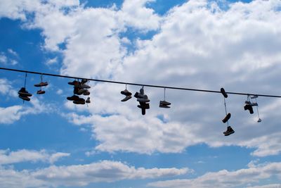 Low angle view of cables and shoes hanging against sky