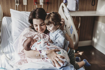 Mid view of mother holding newborn son meeting siblings