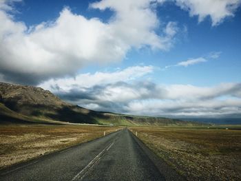 Road passing through landscape against cloudy sky