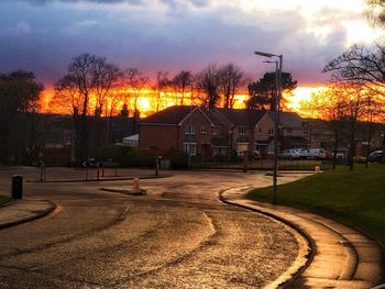 Street by buildings against sky during sunset