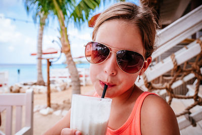 Portrait of girl drinking smoothie while standing at beach