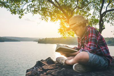 Midsection of boy sitting by lake against sky
