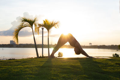 Woman exercising against lake in park during sunset