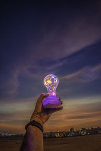 Person holding illuminated lighting equipment against sky during sunset