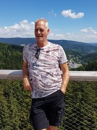 Smiling mature man looking away while standing by railing against mountains during sunny day