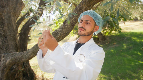 Man with lab coat checking the health of an olive tree touching with hands