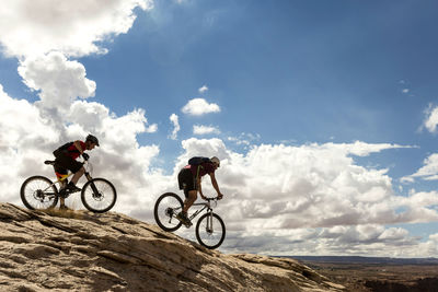 Side view of mountain bikers riding bicycles against cloudy sky