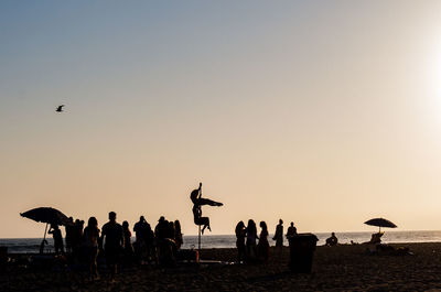 People enjoying at beach against sky during sunset