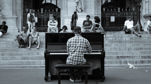 Rear view of man playing piano on city street
