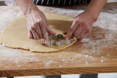 Cropped hands of chef cutting dough with pastry cutter at table