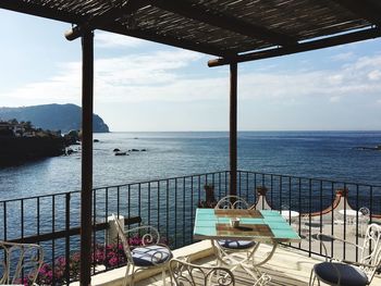 Chairs and table by sea against sky