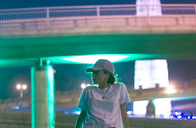 Woman standing against bridge in city at night