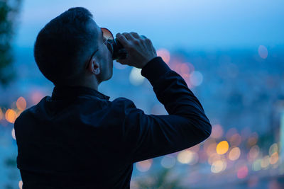 Rear view of man having drink at dusk