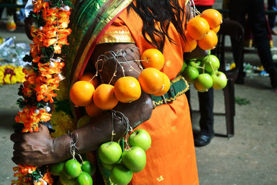 Midsection of woman with pierced fruits and garlands during festival