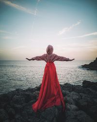 Rear view of person on rock at beach during sunset