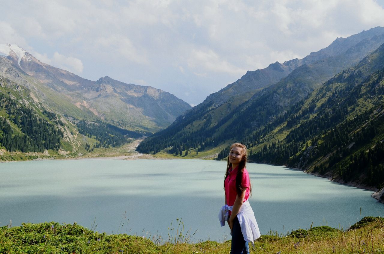 standing, mountain, casual clothing, leisure activity, mountain range, lifestyles, scenics, long hair, full length, tranquil scene, tranquility, sky, lake, young adult, beauty in nature, person, young women, cloud - sky, non-urban scene, nature, vacations, green color, in front of, day, weekend activities