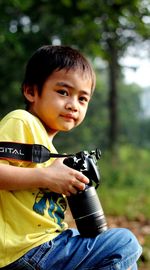 Portrait of cute boy holding camera outdoors