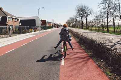 Rear view of woman riding bicycle on street against sky