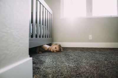 Portrait of shirtless boy lying on rug under bed at home