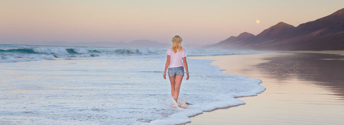 Rear view of woman standing on beach during sunset