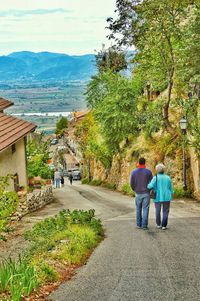 Rear view of people walking on road along trees