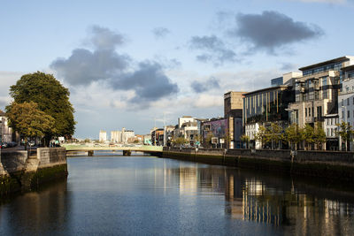 Bridge over river by buildings in city against sky