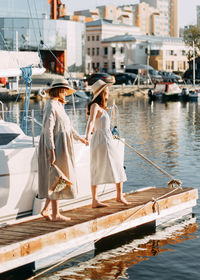 Two women friends walk along the pier along the boats and yachts in summer