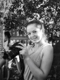 Portrait of woman smiling while photographing with camera against branches