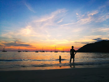 Silhouette people on beach against sky during sunset