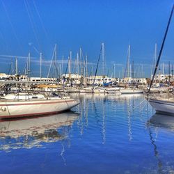 Sailboats moored on sea against blue sky