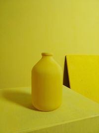 Close-up of yellow bottle on table against wall