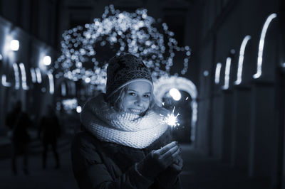 Smiling woman holding lit sparkler at night