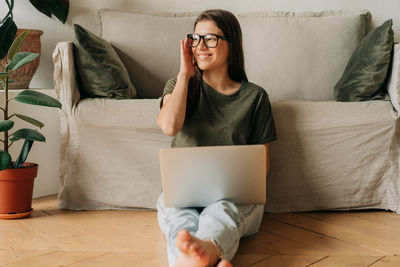 Young woman using laptop while sitting on sofa at home