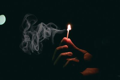 Close-up of hand holding lit candle against black background