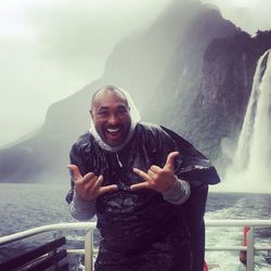 Portrait of smiling man gesturing while standing against waterfall in sea