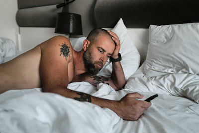 Tattooed man laying in bed using phone