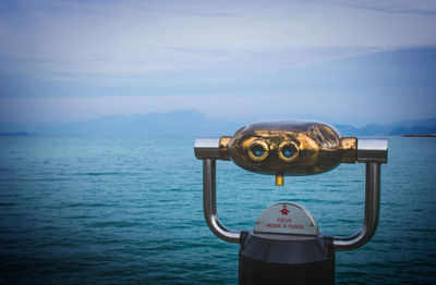 Coin-operated binoculars by sea against sky