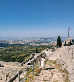 Front view of woman standing on top of klis fortress overlooking coastal city of split in croatia.