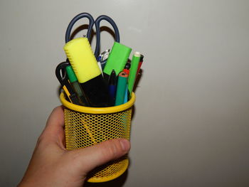 Cropped hand of person holding school supplies against wall