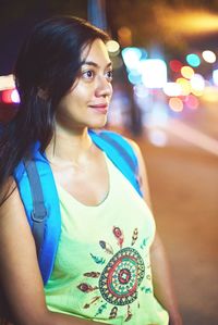 Young woman looking away while standing in illuminated city