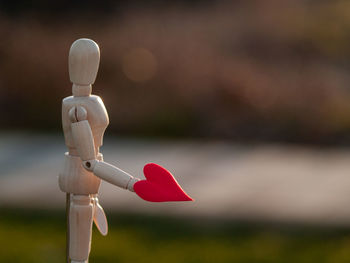 Close-up of wooden figurine holding red heart shape