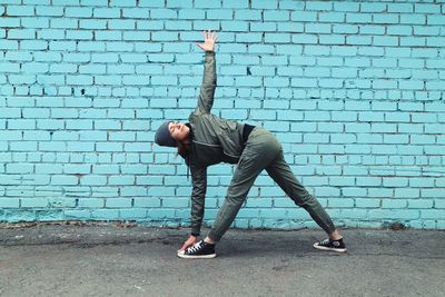 Young woman exercising on road while standing against wall