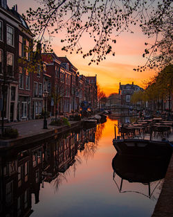 Boats moored in river by buildings against sky during sunset