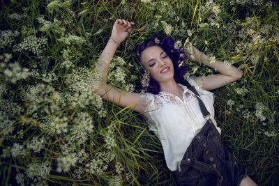 Portrait of a teenage girl with purple hair and an earring in her nose lying in the grass in nature