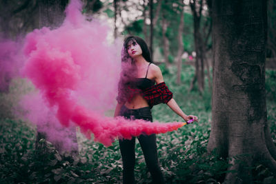 Portrait of young woman standing by pink tree in forest