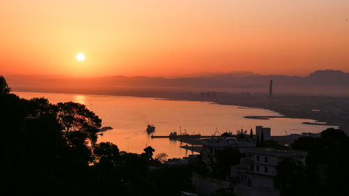 High angle view of silhouette buildings by sea against romantic sky