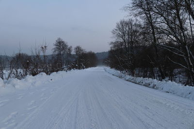 Snow covered road amidst trees against sky during winter