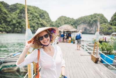 Portrait of smiling woman wearing sunglasses and hat on pier
